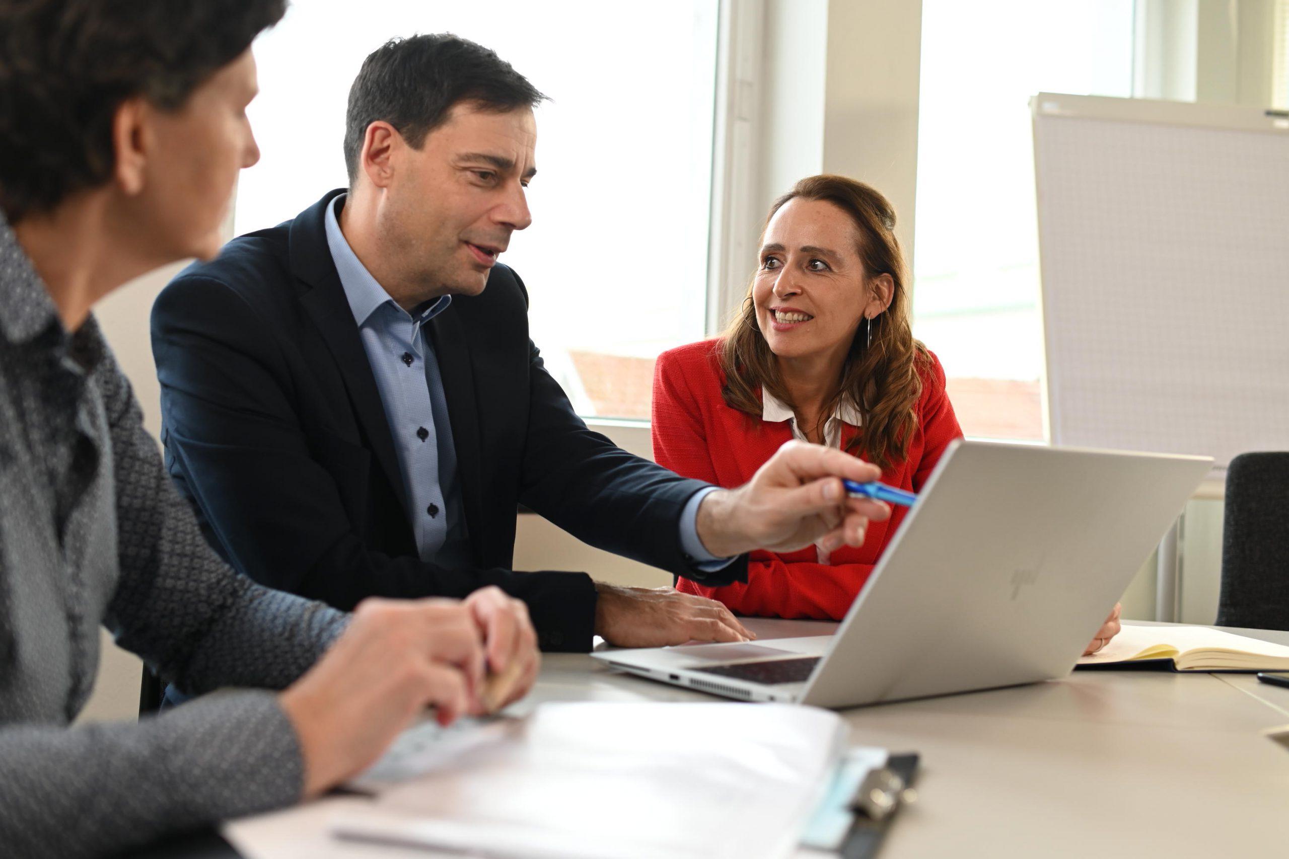 Two men and a woman looking at a laptop and talking